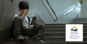 A child sits on stairs, looking at a smartphone, with one hand on head, displaying a distressed expression. Nearby is a logo for the British Columbia Ministry of Children and Family Development.